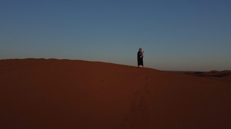 A lone traveller on the high dune ridge at sunset in the Moroccan Sahara