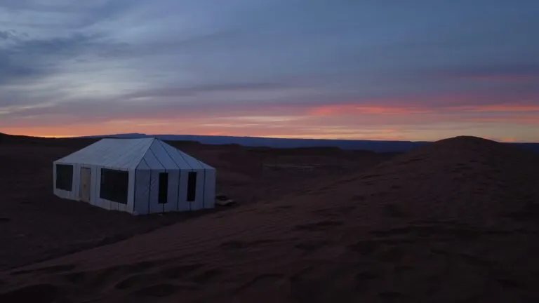 A single canvas tent pitched on the dune crest at twilight