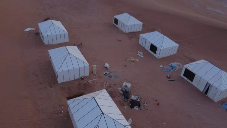 Cluster of white desert tents on the sand seen from overhead