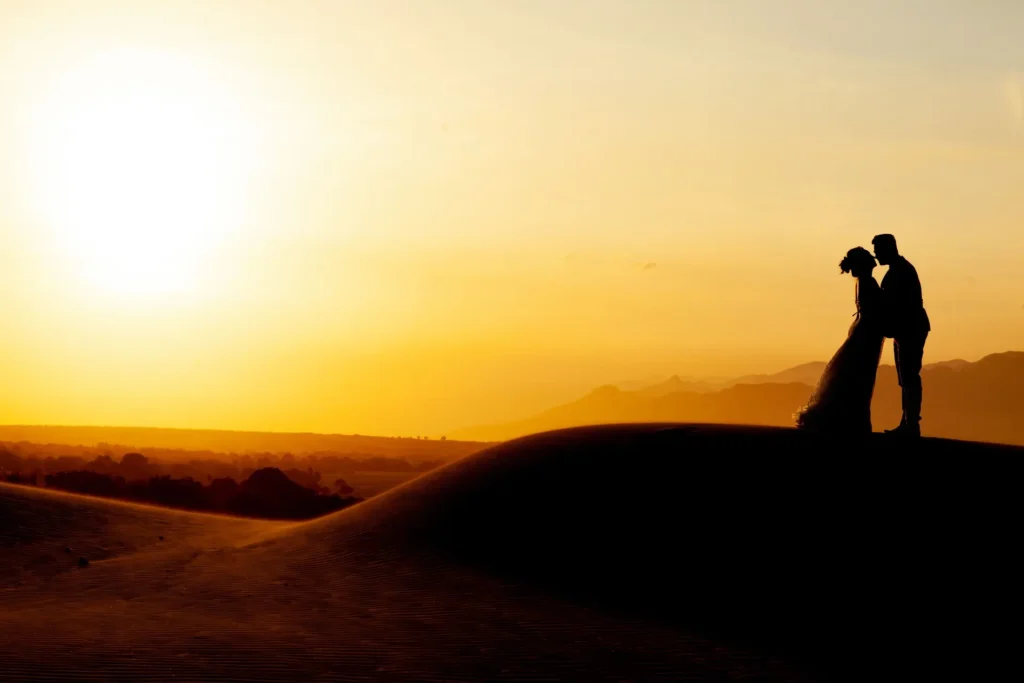 Honeymoon couple silhouetted on desert dunes at sunset