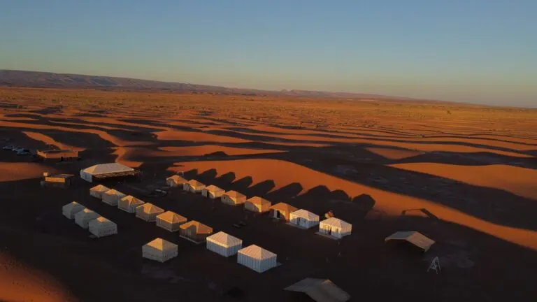 Rows of desert tents beneath a dune ridge at twilight