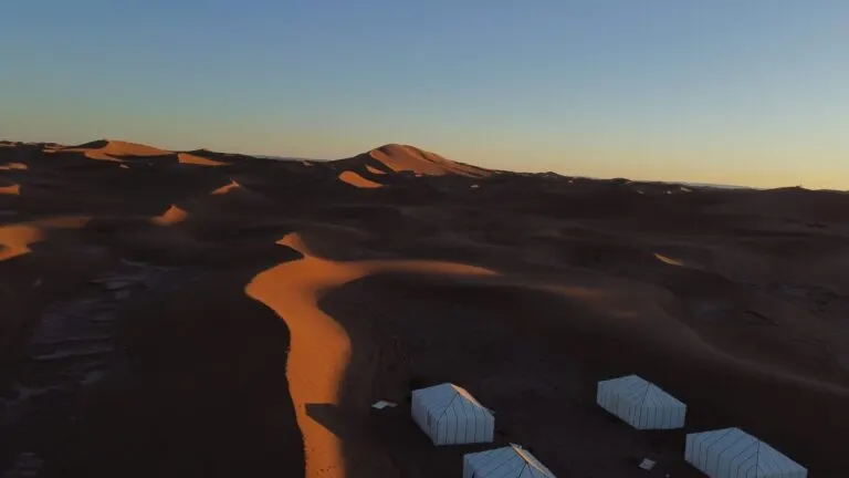 Desert camp scattered across the dunes at Erg Chegaga in blue hour light