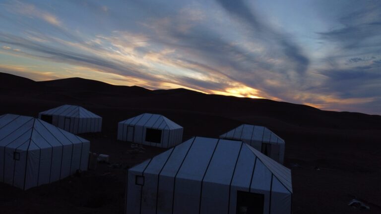 Desert camp at dawn beneath a wide band of cloud over the Sahara
