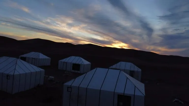 Desert camp at dawn beneath a wide band of cloud over the Sahara